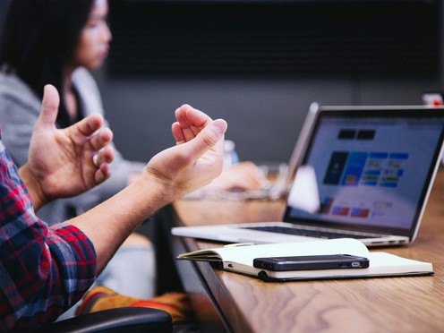 Photo of a meeting with people talking in front of a laptop displaying an interface.